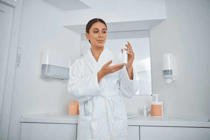 Elegant woman in a robe selecting skincare products from a lineup in front of a mirror, possibly as part of her beauty regimen post Dermalax filler treatment