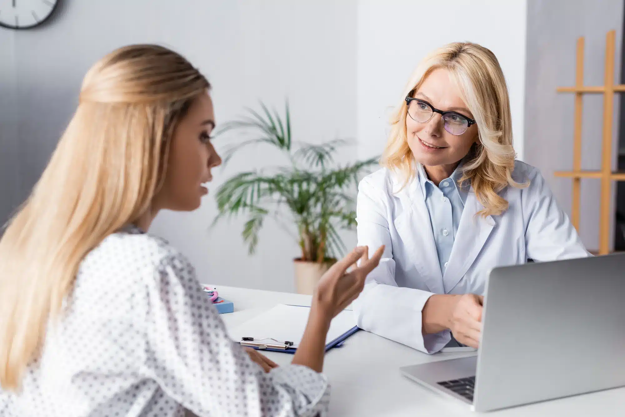 Doctor patient consultation before plastic surgery. Patient is looking at the doctors laptop with surgery results simulation.
