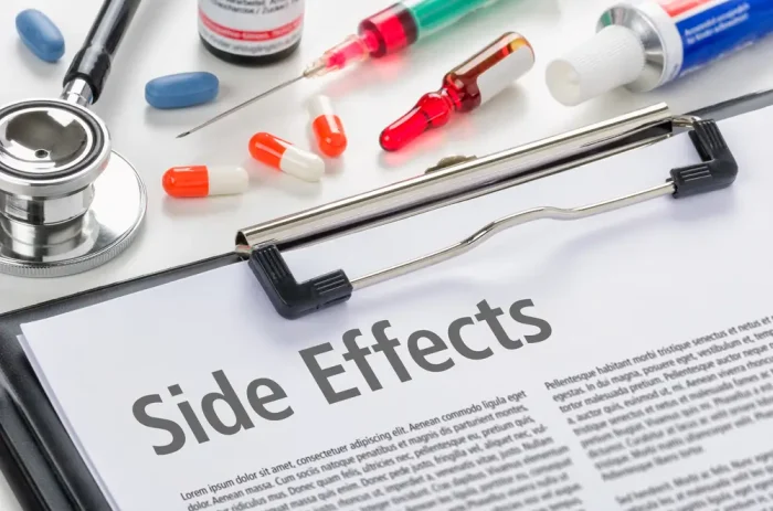 A clipboard labeled "Side Effects" surrounded by various medicines, including pills, capsules, a syringe, a tube, and a stethoscope.