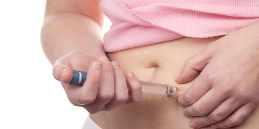 A person wearing a pink top injects medication into their abdomen with a syringe.