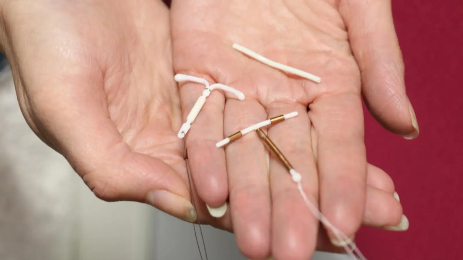 A close-up of two hands holding three different types of intrauterine devices (IUDs) used for birth control, including both hormonal and copper options.