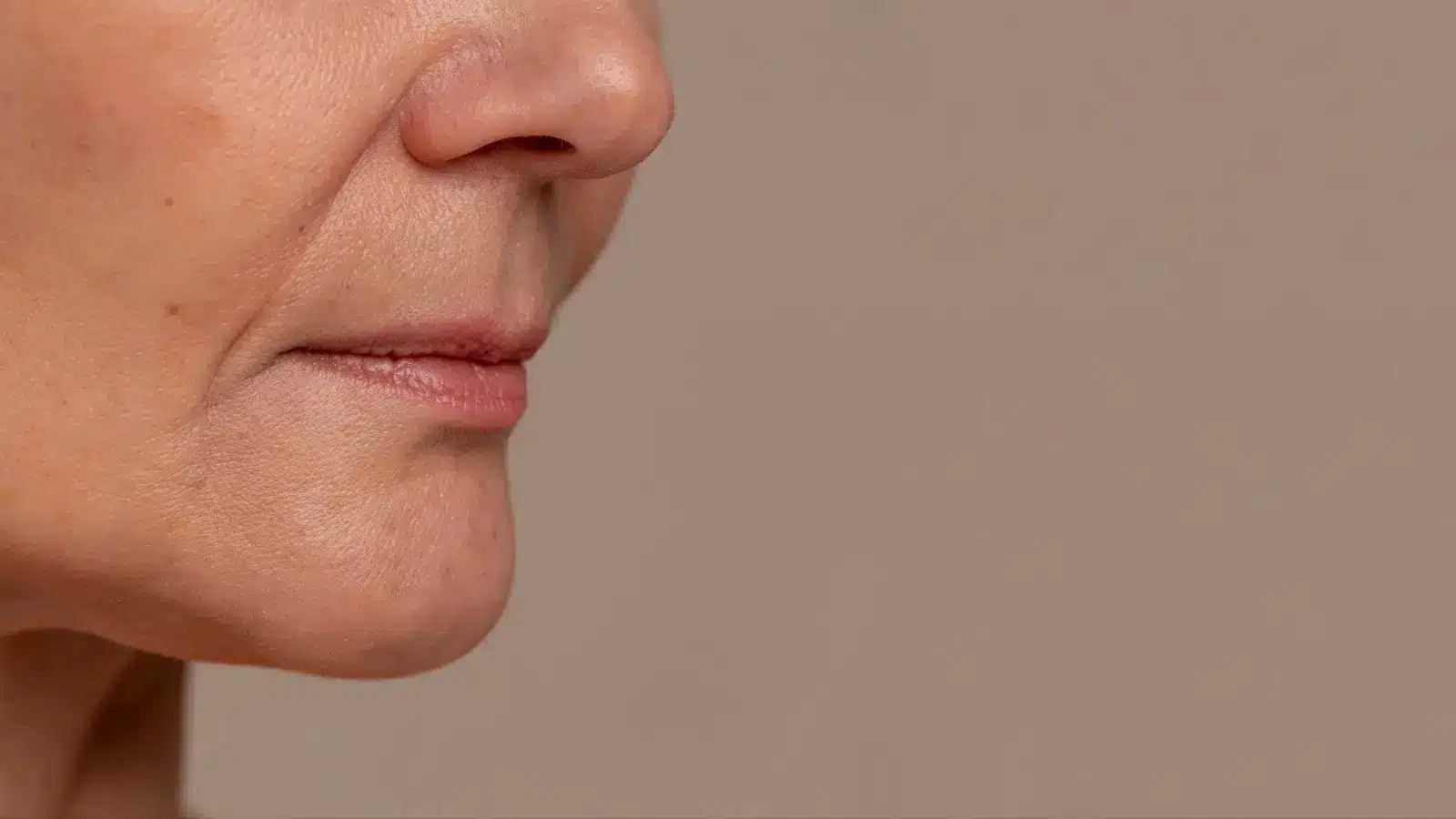 Close-up of the lower half of an older adult's face with visible wrinkles and fine lines around the mouth and chin, set against a neutral background.
