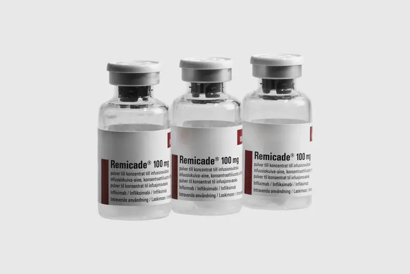 Three glass vials labeled "Remicade 100 mg" are standing upright on a plain white background. The vials have gray caps and visible labels with black and red text.