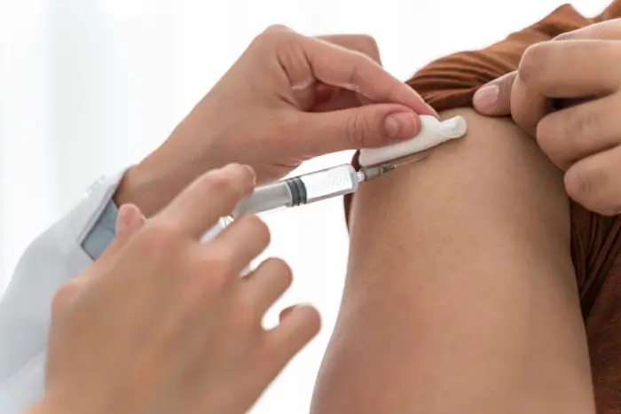 A close-up of a healthcare worker administering a Xolair injection into a person’s upper arm, with a cotton ball held on the skin.