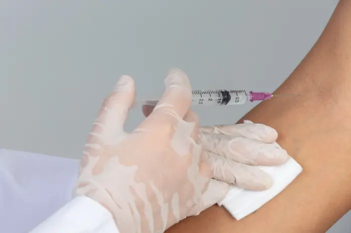 A close-up of gloved hands preparing to inject Xolair into a person's arm, with a cotton pad held against the skin.
