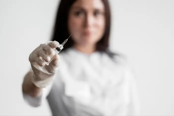 A woman wearing medical gloves holds a Xolair syringe towards the camera, with the focus on the syringe and her face blurred in the background.