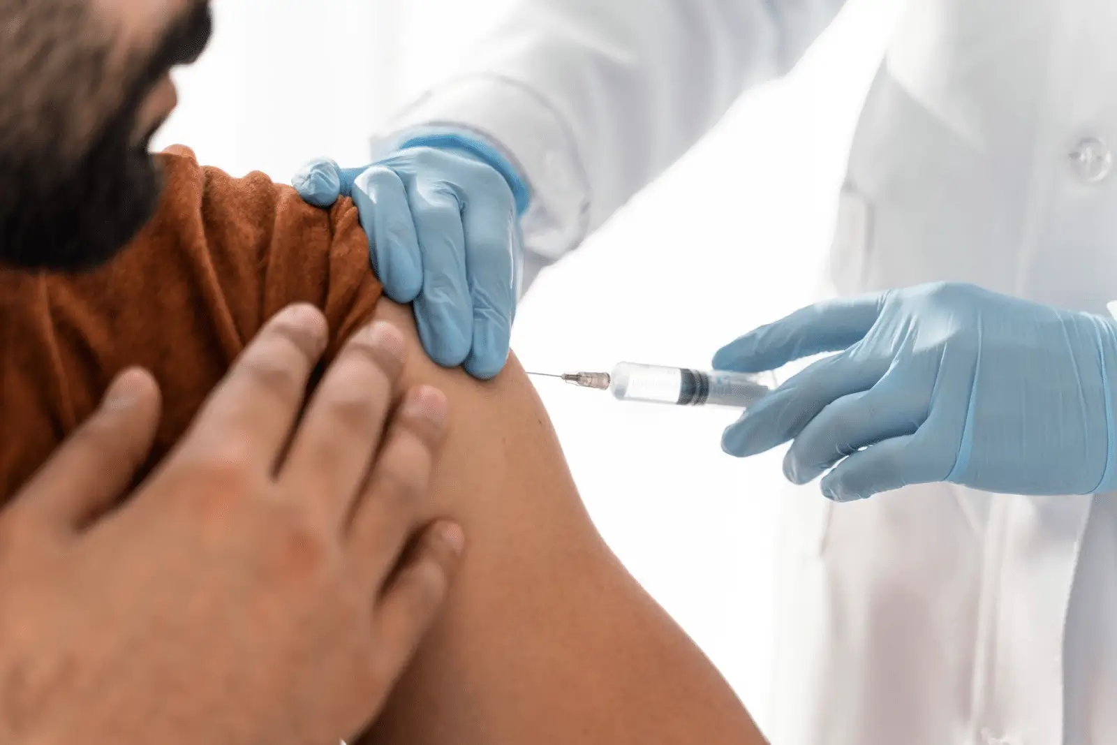 A healthcare professional wearing blue gloves administers a Xolair injection into a person's upper arm. The person receiving the treatment is wearing a brown shirt and holding their shoulder.