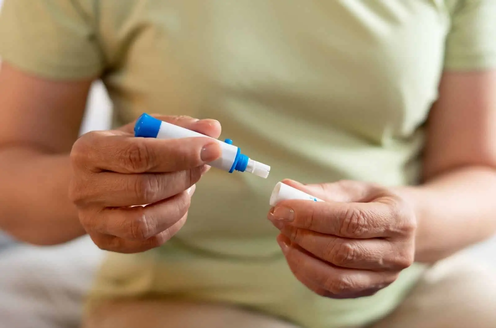 A person wearing a light green shirt holds a pen similar to Mounjaro, with the cap removed and held in the other hand, preparing to use the medication.