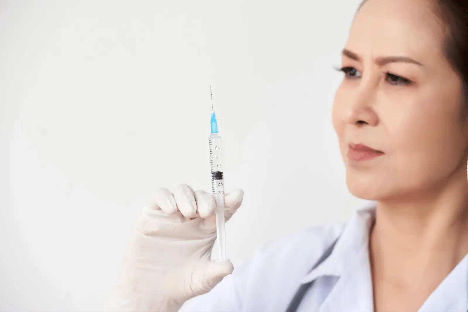 A healthcare professional wearing white gloves holds up a syringe filled with Xolair, examining it closely against a plain, light background.