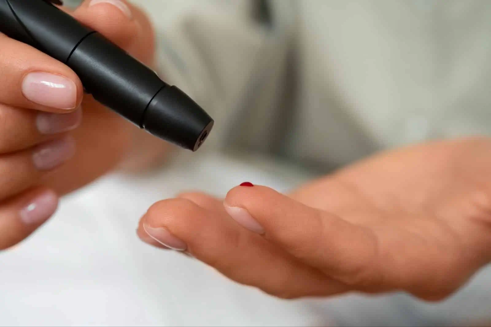 Close-up of a person using a blood glucose meter to prick their finger, with a small drop of blood visible on the fingertip. This to check blood sugar before Mounjaro treatment.